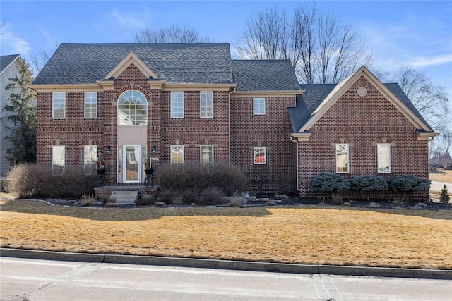 view of front facade featuring brick siding, a front lawn, and roof with shingles