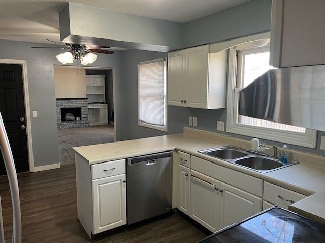 kitchen with a brick fireplace, stainless steel dishwasher, kitchen peninsula, sink, and white cabinets