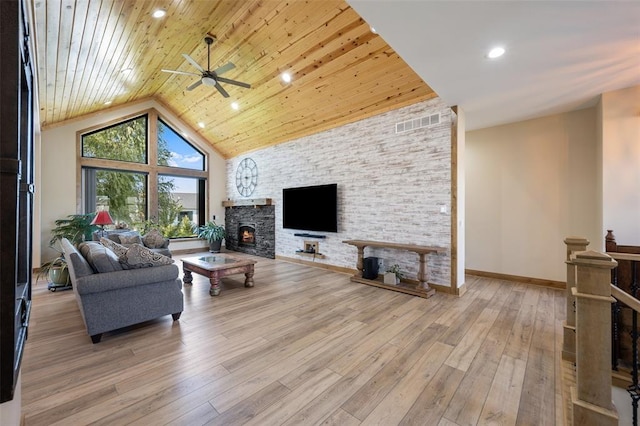 living room with ceiling fan, a fireplace, a towering ceiling, and light hardwood / wood-style floors