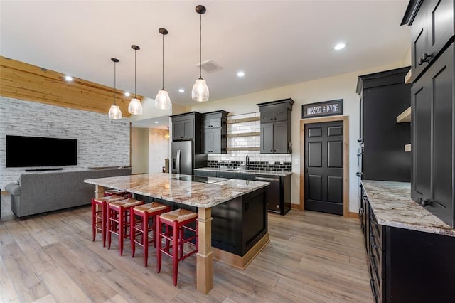 kitchen with a large island with sink, a breakfast bar, stainless steel refrigerator with ice dispenser, sink, and hanging light fixtures