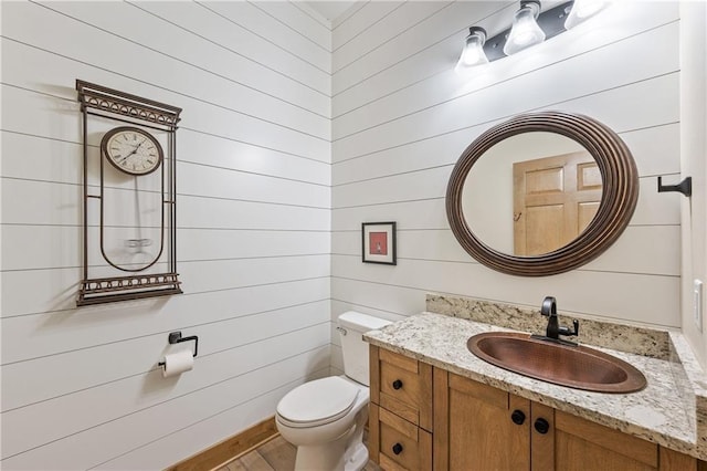 bathroom with toilet, vanity, and wooden walls