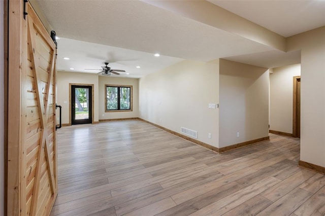 unfurnished room with ceiling fan, a barn door, and light hardwood / wood-style flooring