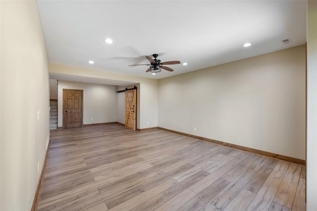 unfurnished room featuring ceiling fan, a barn door, and light wood-type flooring