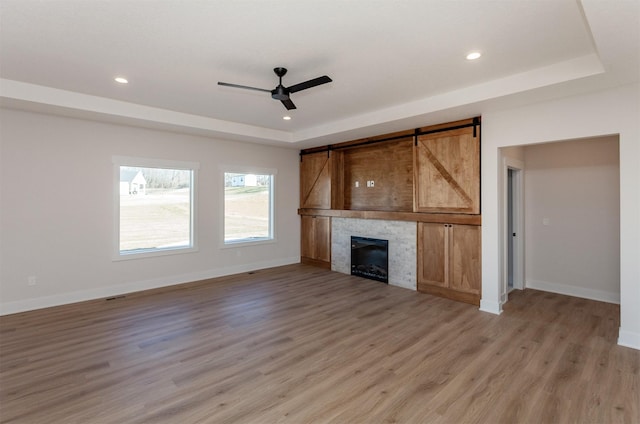 unfurnished living room with ceiling fan, a fireplace, hardwood / wood-style floors, and a tray ceiling