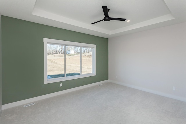 empty room with ceiling fan, light colored carpet, and a tray ceiling