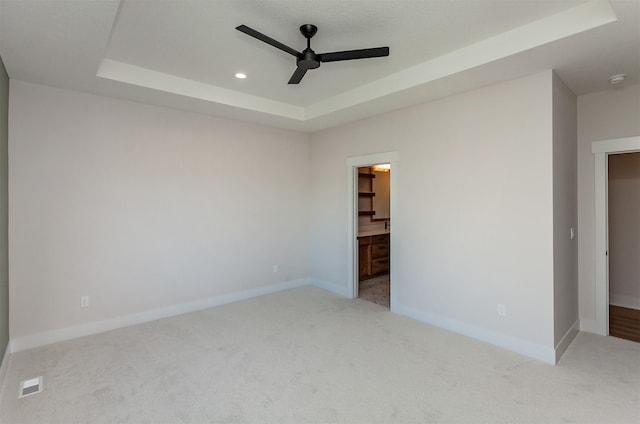 unfurnished bedroom featuring ceiling fan, light colored carpet, ensuite bathroom, and a raised ceiling