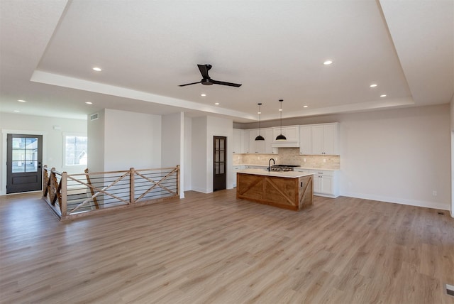 kitchen with white cabinets, sink, a large island, a raised ceiling, and light hardwood / wood-style flooring