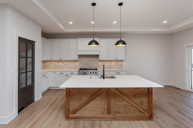 kitchen featuring a center island with sink, stove, pendant lighting, white cabinets, and sink