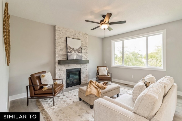 living room featuring ceiling fan, a stone fireplace, and light wood-type flooring