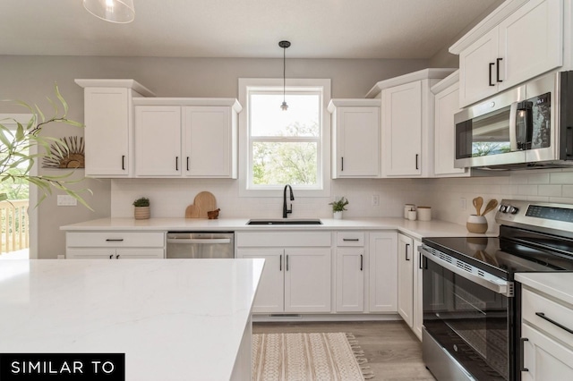 kitchen featuring sink, white cabinetry, hanging light fixtures, light wood-type flooring, and appliances with stainless steel finishes