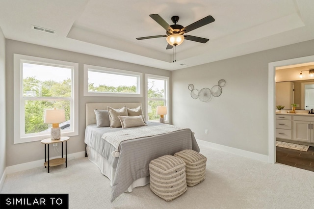 carpeted bedroom featuring ceiling fan, ensuite bathroom, a raised ceiling, and multiple windows