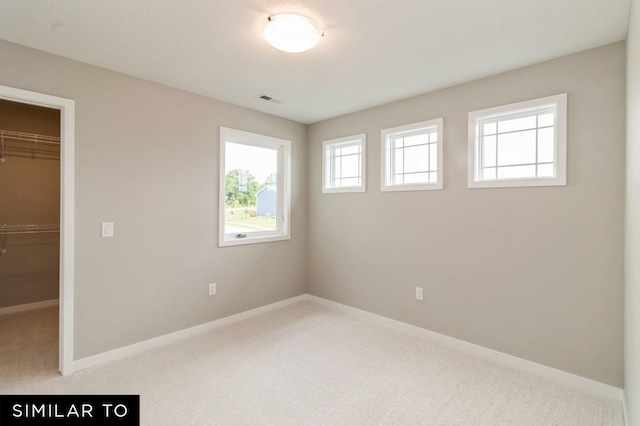 unfurnished bedroom with a walk in closet, a closet, light colored carpet, and multiple windows