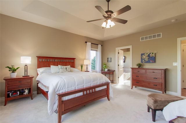 bedroom with ceiling fan, ensuite bath, light carpet, and a tray ceiling