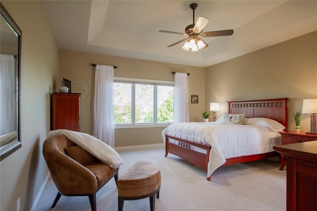 bedroom with light carpet, ceiling fan, and a raised ceiling