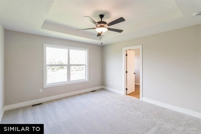 unfurnished room featuring a raised ceiling, light carpet, and ceiling fan