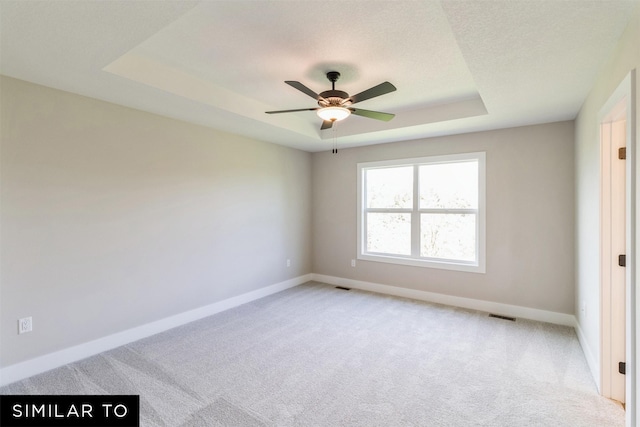 spare room featuring ceiling fan, light carpet, and a raised ceiling