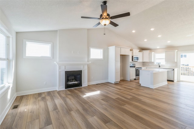 4207 NE 3rd St, Ankeny, IA 50021 - unfurnished living room with vaulted ceiling, visible vents, a ceiling fan, a glass covered fireplace, and light wood-style flooring