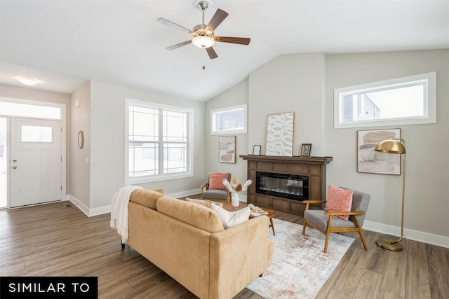 living room with ceiling fan, baseboards, vaulted ceiling, wood finished floors, and a glass covered fireplace