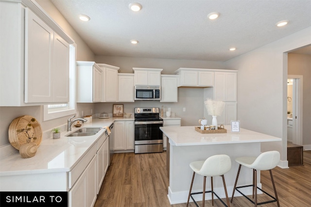 kitchen with white cabinetry, stainless steel appliances, a center island, light wood-type flooring, and sink