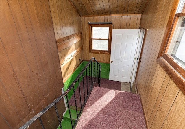 hallway with wooden ceiling, wood walls, and dark colored carpet