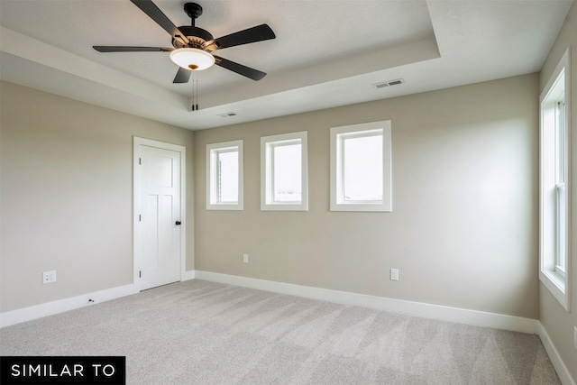 empty room with ceiling fan, light carpet, and a tray ceiling