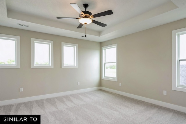 carpeted spare room with a raised ceiling and ceiling fan