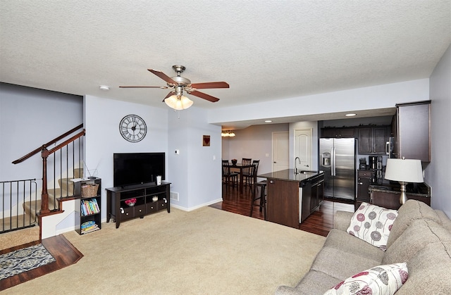 living area with baseboards, ceiling fan, stairs, a textured ceiling, and carpet flooring