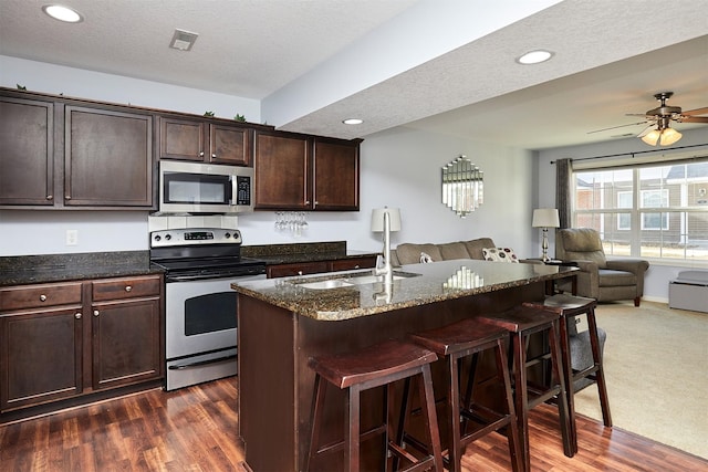 kitchen with visible vents, dark stone countertops, a kitchen breakfast bar, open floor plan, and stainless steel appliances