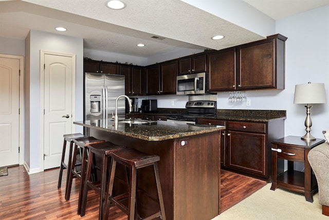 kitchen featuring visible vents, a sink, dark wood-type flooring, appliances with stainless steel finishes, and a kitchen bar