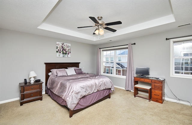 bedroom with visible vents, light colored carpet, and a raised ceiling