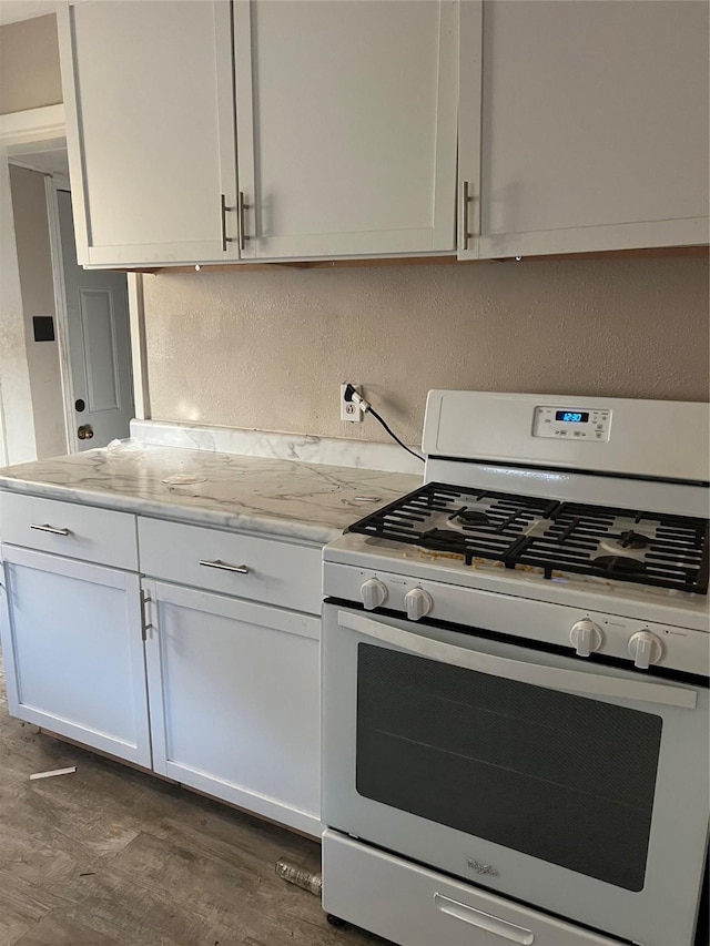 kitchen featuring dark wood-type flooring, white cabinets, light stone counters, and white gas stove