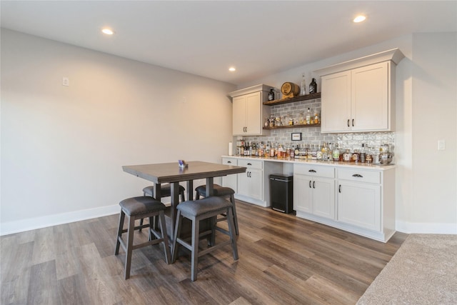 bar featuring dark wood-type flooring, white cabinets, and tasteful backsplash