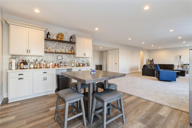 kitchen featuring white cabinetry, light hardwood / wood-style floors, tasteful backsplash, and a kitchen bar