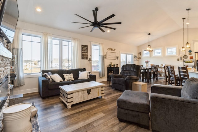 living room featuring lofted ceiling, dark hardwood / wood-style flooring, ceiling fan with notable chandelier, and a stone fireplace