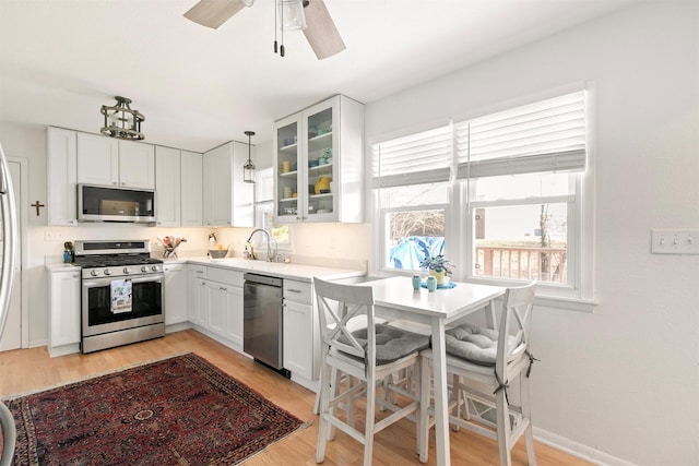 kitchen featuring decorative light fixtures, sink, white cabinetry, light wood-type flooring, and appliances with stainless steel finishes