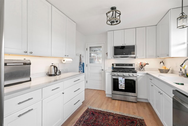 kitchen with white cabinetry, stainless steel appliances, light wood-type flooring, hanging light fixtures, and sink