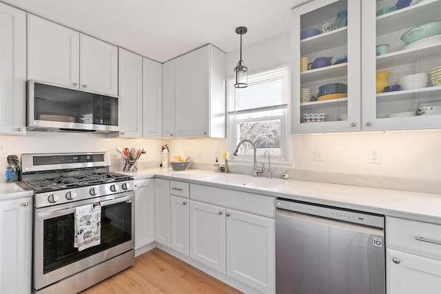 kitchen featuring pendant lighting, sink, light hardwood / wood-style flooring, appliances with stainless steel finishes, and white cabinets