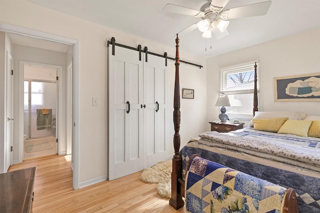 bedroom featuring ceiling fan, light hardwood / wood-style floors, ensuite bath, and a barn door