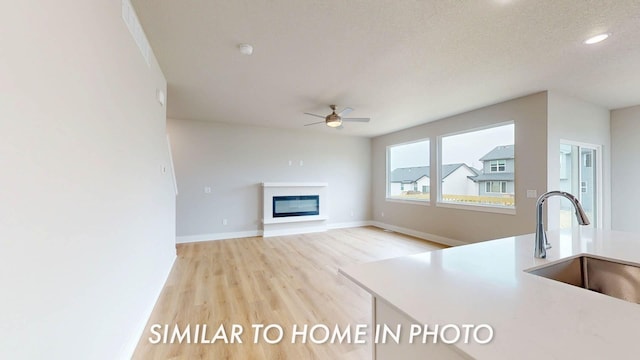 503 43rd St SW, Altoona, IA 50009 - unfurnished living room featuring ceiling fan, a sink, a glass covered fireplace, baseboards, and light wood-type flooring