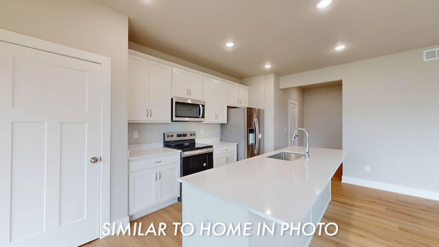 503 43rd St SW, Altoona, IA 50009 - kitchen with white cabinets, a sink, light wood finished floors, a kitchen island with sink, and stainless steel appliances