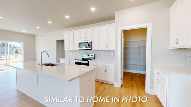 kitchen with stainless steel appliances, an island with sink, sink, and white cabinets