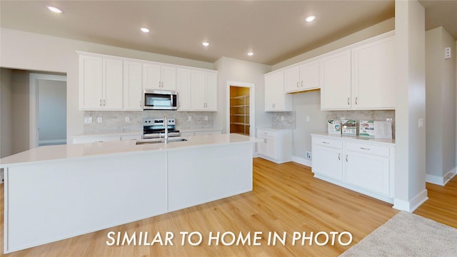 kitchen with white cabinetry, sink, stainless steel appliances, and a center island with sink