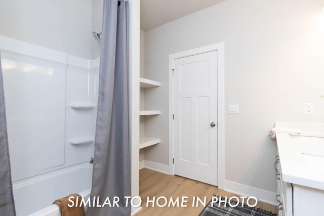 full bath featuring shower / tub combo, baseboards, vanity, and wood finished floors