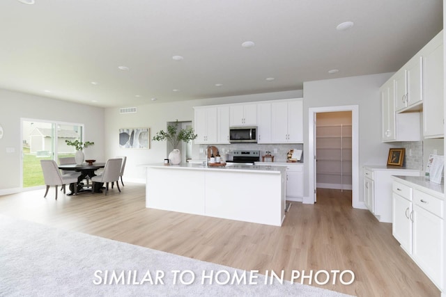 kitchen with white cabinets, light wood finished floors, tasteful backsplash, and appliances with stainless steel finishes