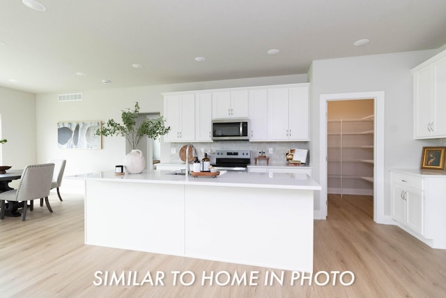 kitchen featuring white cabinets, light wood finished floors, stainless steel appliances, backsplash, and light countertops