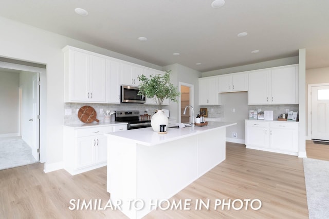 kitchen with light wood finished floors, stainless steel appliances, backsplash, a sink, and white cabinetry