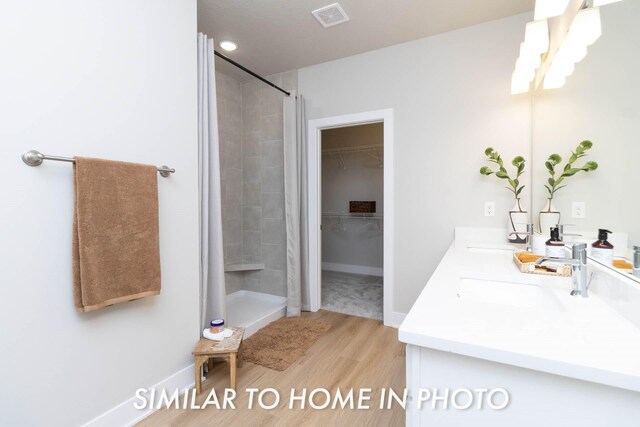 bathroom featuring a sink, double vanity, a stall shower, visible vents, and wood finished floors