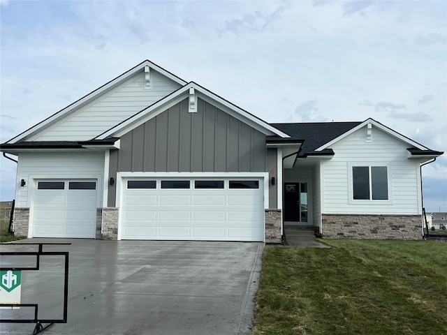 view of front of house with an attached garage, driveway, stone siding, and a front lawn