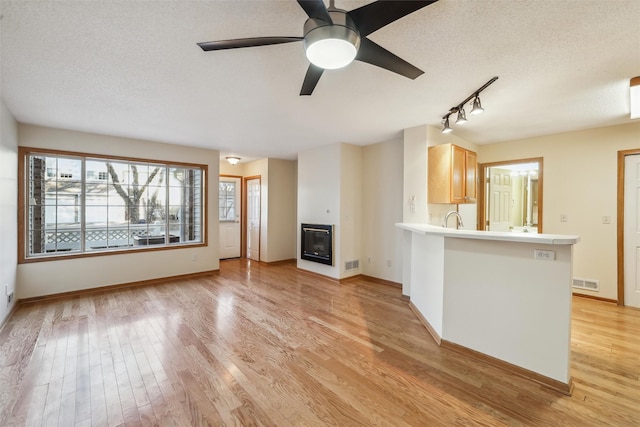 unfurnished living room featuring ceiling fan, rail lighting, a textured ceiling, and light wood-type flooring