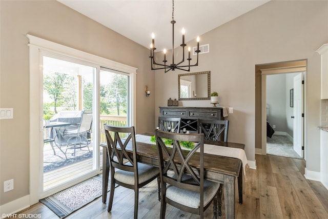 dining room featuring light wood-type flooring, vaulted ceiling, and a notable chandelier